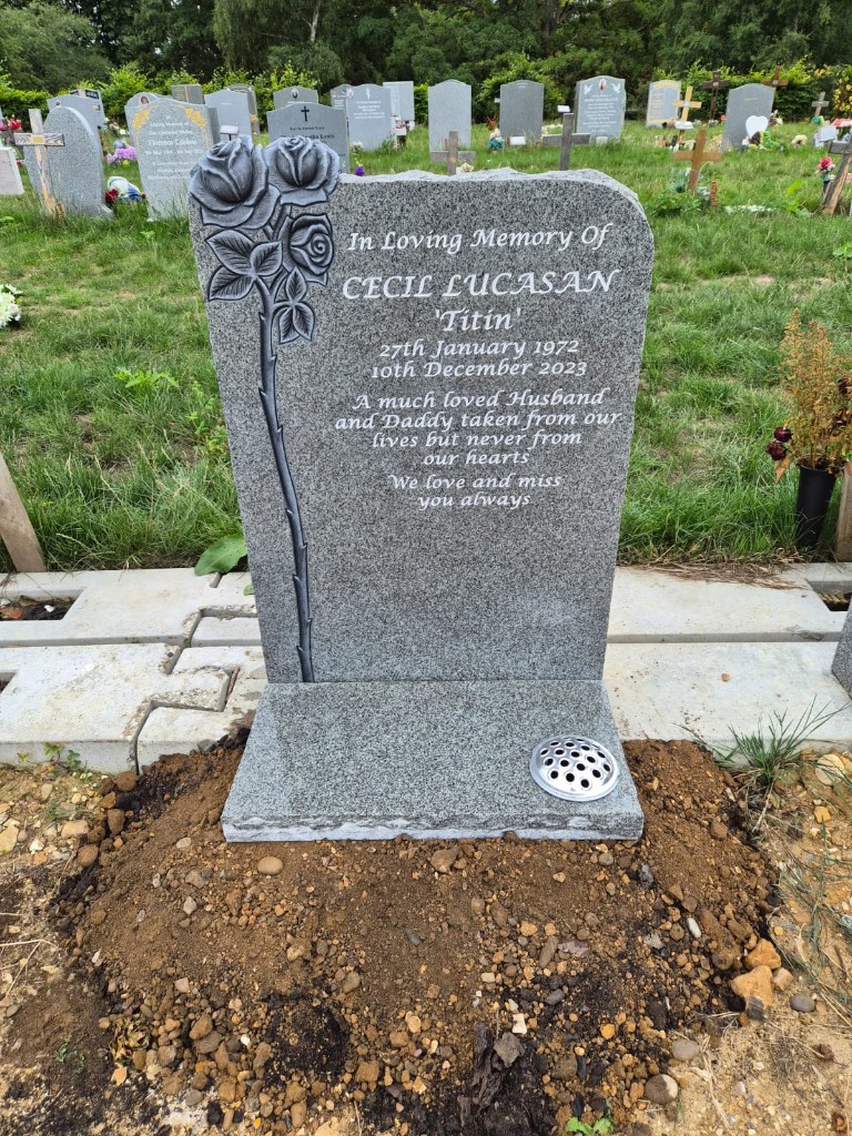 Polished grey speckled granite lawn memorial with carved long-stem rose, pale engraved lettering and integrated metal flower holder on base at City of London Cemetery, East London — memorial installation