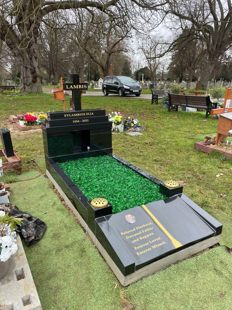 Polished black granite full kerb memorial with cross headstone, green glass chippings, open book footstone with ceramic portrait and gold lettering at Edmonton Cemetery, North London — memorial installation