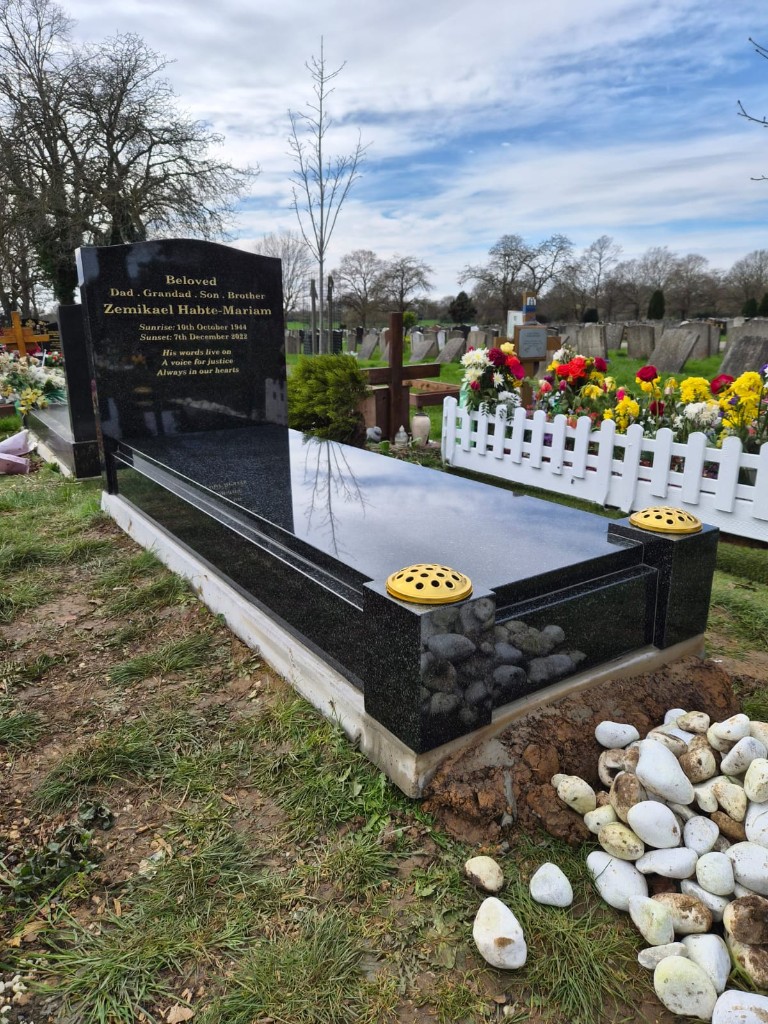 Polished black granite full kerb memorial with curved-top headstone, full-length ledger and twin flower vase posts at Edmonton Cemetery, North London, memorial installation