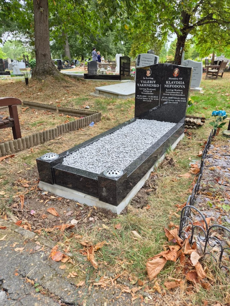 Polished black granite double memorial with curved arch headstone, twin ceramic portrait plaques, etched cross, full kerb set with light grey chippings and flower vase posts at Hendon Cemetery, North London, memorial installation