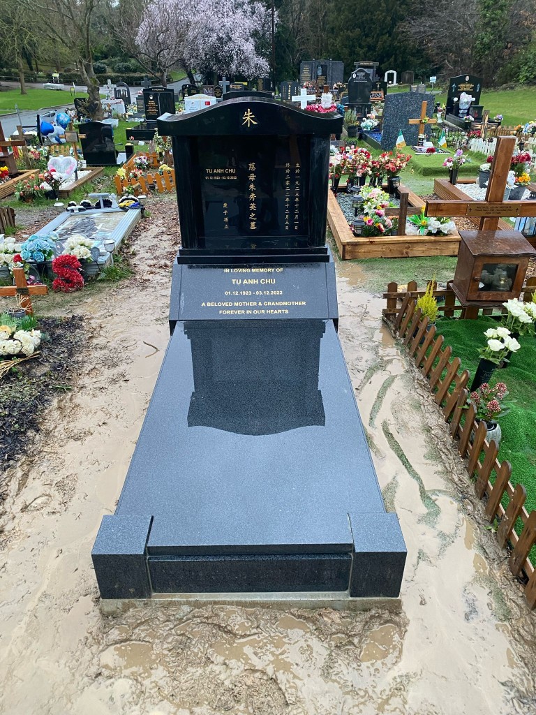 Polished black granite upright memorial with gold bilingual Chinese and English lettering and full-length ledger slab at St Pancras and Islington Cemetery, North London — memorial installation