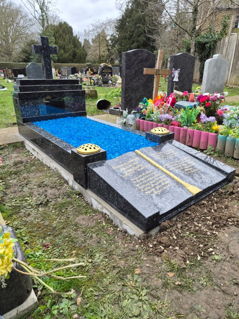 Polished dark speckled granite full kerb memorial with cross headstone, blue glass chippings and open book ledger at Tottenham Cemetery, North London, memorial installation